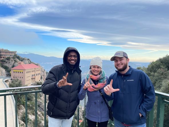 A faculty member and two LSU students are dressed warmly as they smile at the camera holding up Ls.